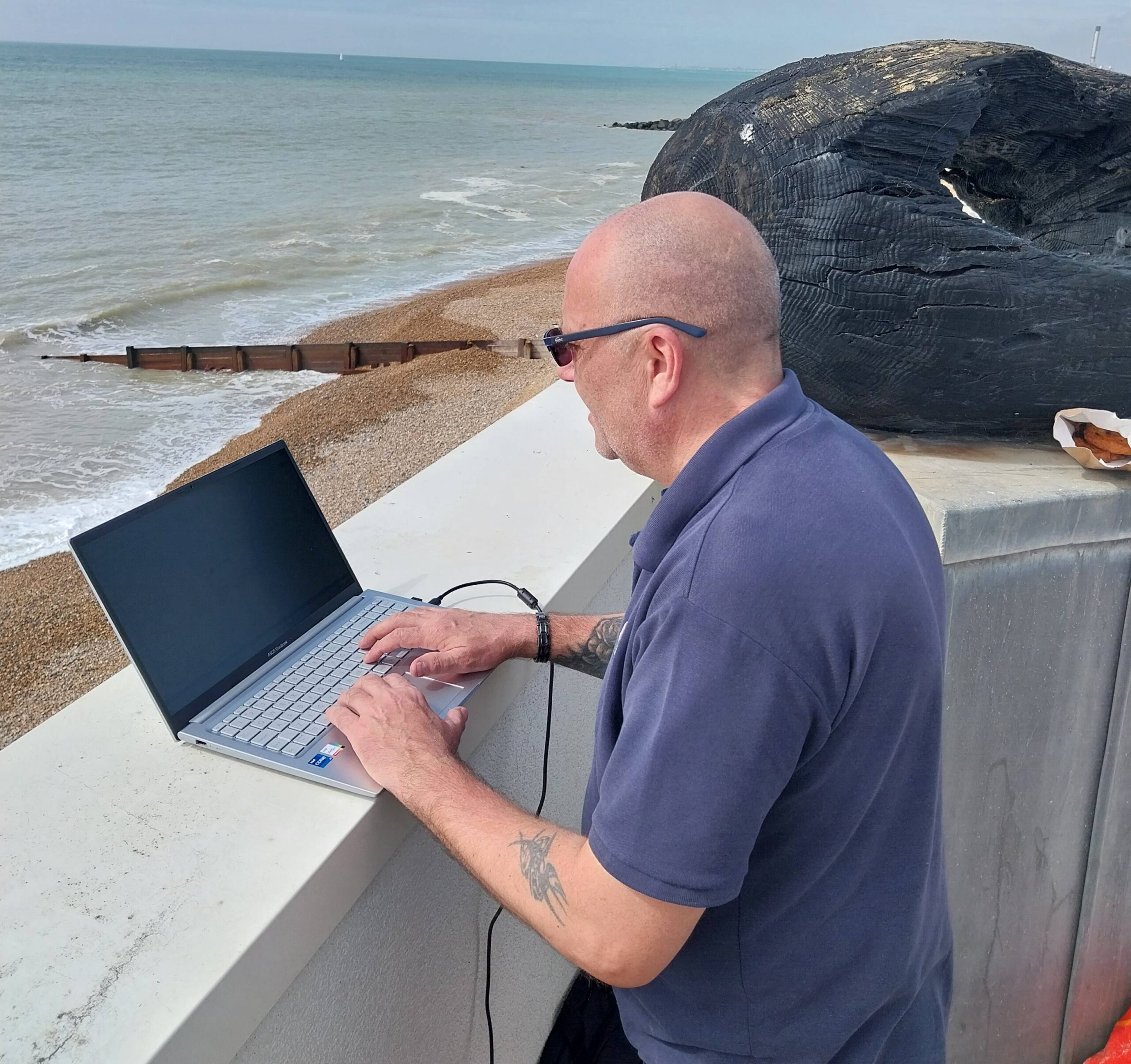 Man working on a laptop by the seaside with a face mask.